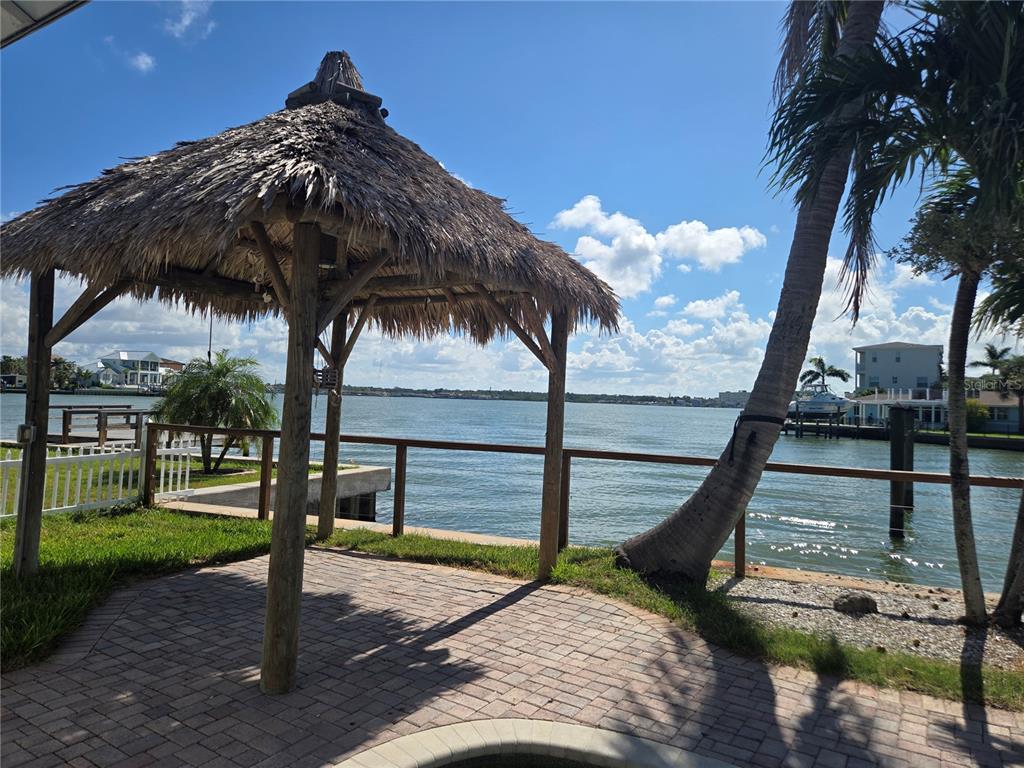 A thatched-roof tiki hut sits on a brick patio overlooking a waterfront canal — 16029 REDINGTON DRIVE, REDINGTON BEACH, FL