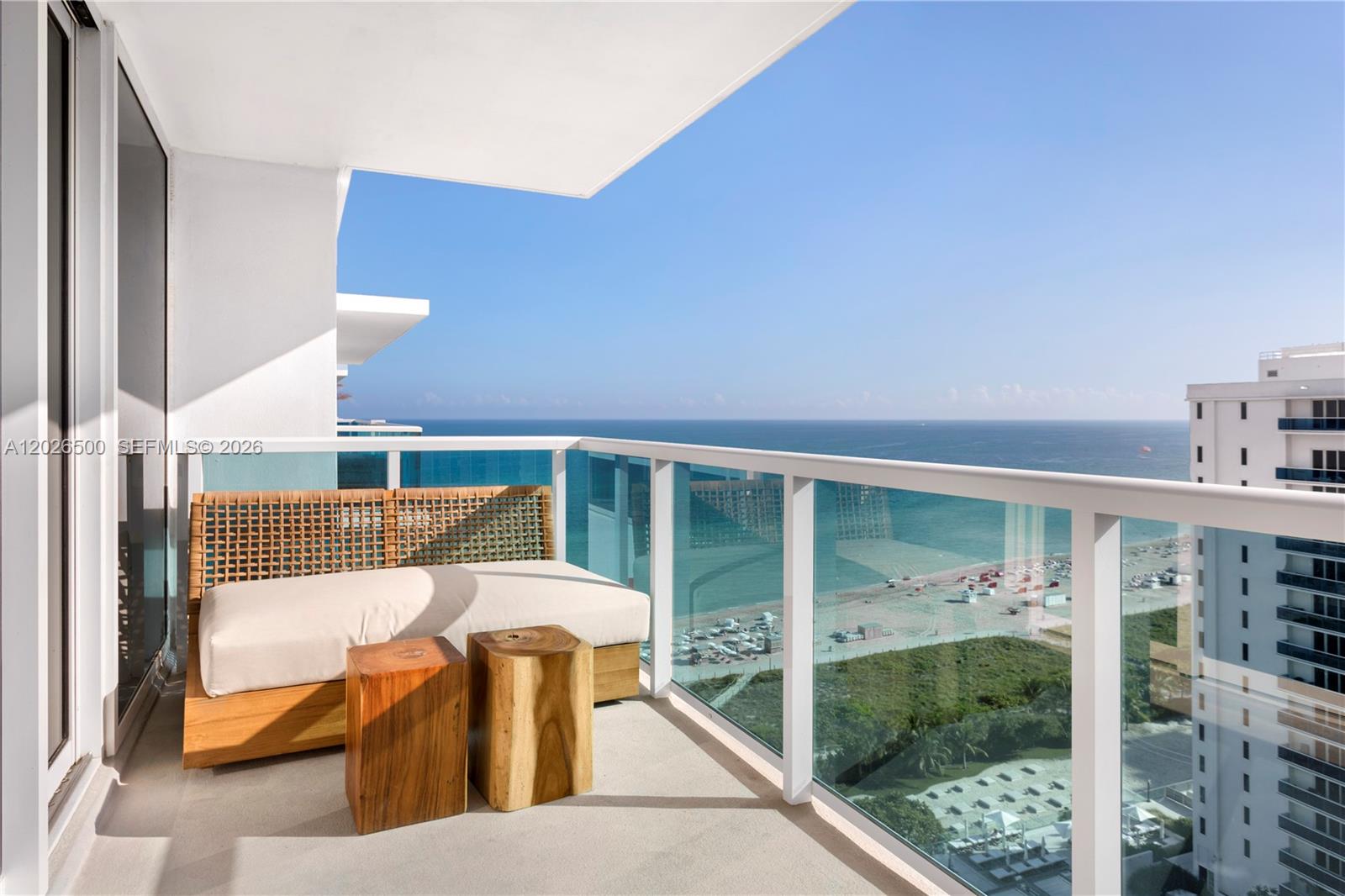 A balcony with a wooden sofa, two stump tables, and a view of the ocean — 102 24th St # 1706, Miami Beach FL 33139, MIAMI BEACH, FL