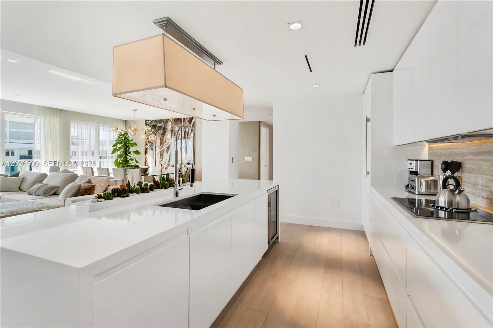 A modern white kitchen features a large island with a sink and a pendant light — 102 24th St # 1706, Miami Beach FL 33139, MIAMI BEACH, FL