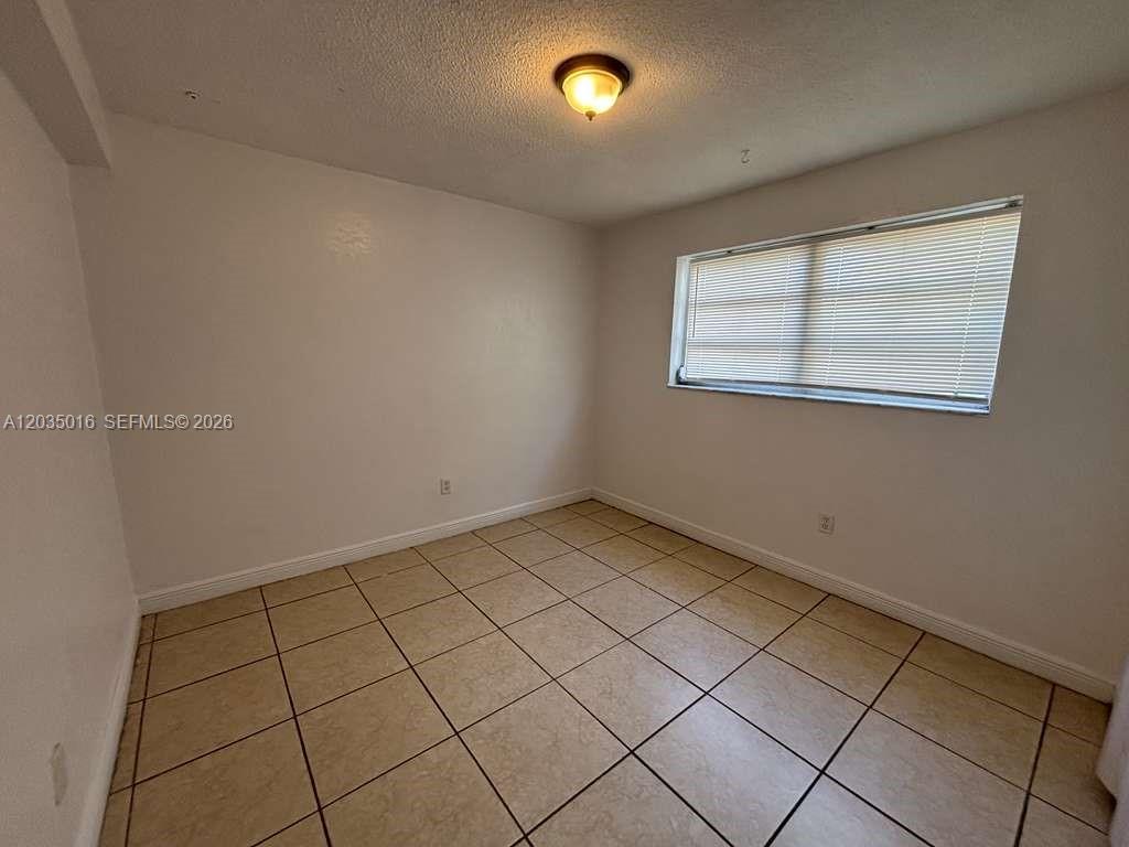 An empty room features light-colored walls, a window with blinds, and beige tiled flooring — 8275 NE Miami Ct # 202, Miami FL 33138, MIAMI, FL
