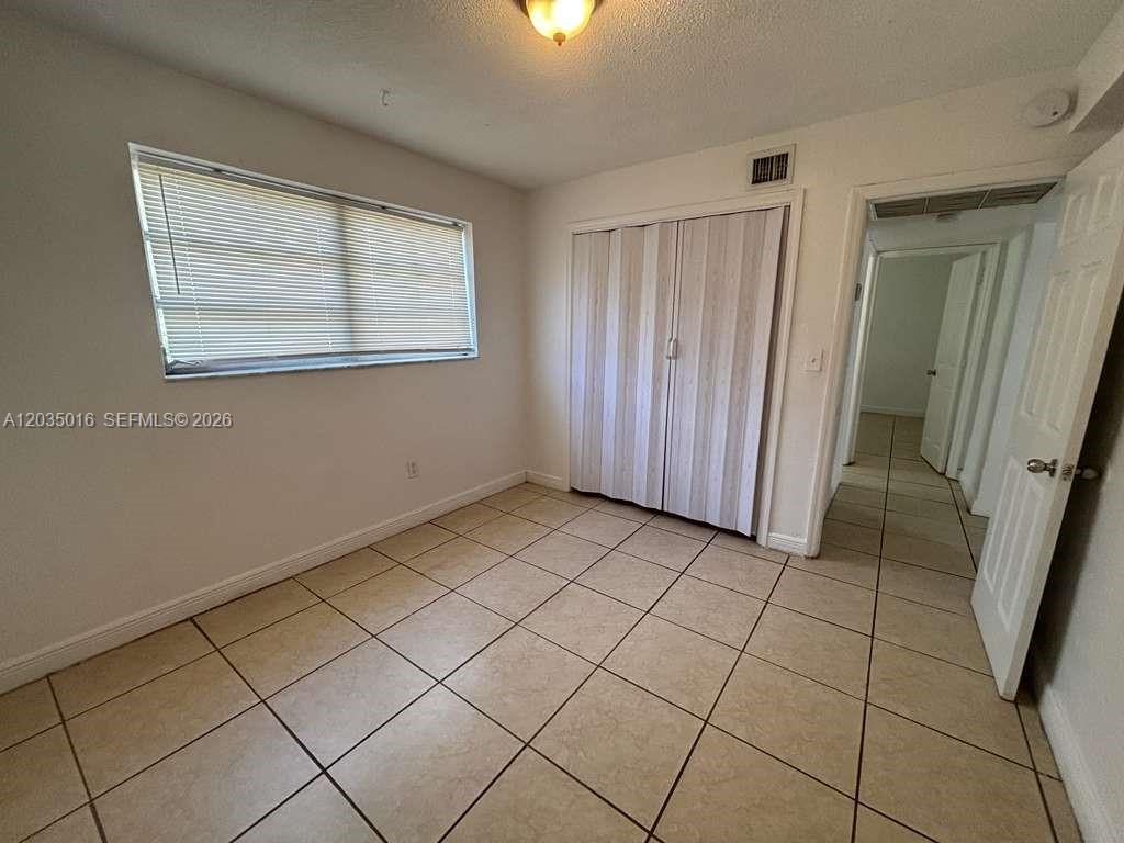 A bedroom features light-colored tile flooring, a window with blinds, and a white closet — 8275 NE Miami Ct # 202, Miami FL 33138, MIAMI, FL