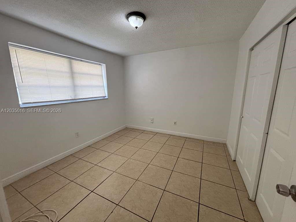 A bedroom features white walls, tile flooring, a window with blinds, and a closet — 8275 NE Miami Ct # 202, Miami FL 33138, MIAMI, FL