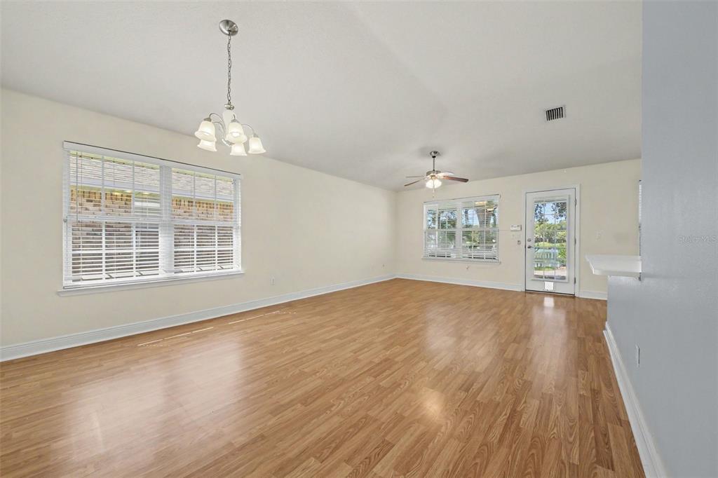 An empty room with light wood-look flooring, a ceiling fan, a chandelier, and two windows — 567 CORAL TRACE BOULEVARD, EDGEWATER, FL