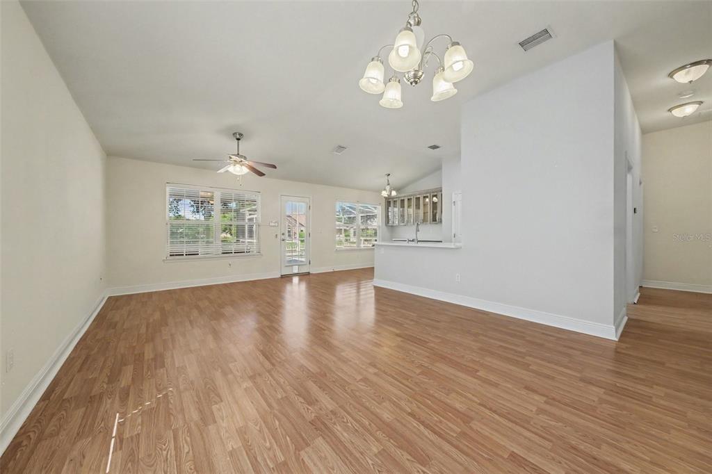 An open-concept living and dining area features light wood-look flooring and a central chandelier — 567 CORAL TRACE BOULEVARD, EDGEWATER, FL