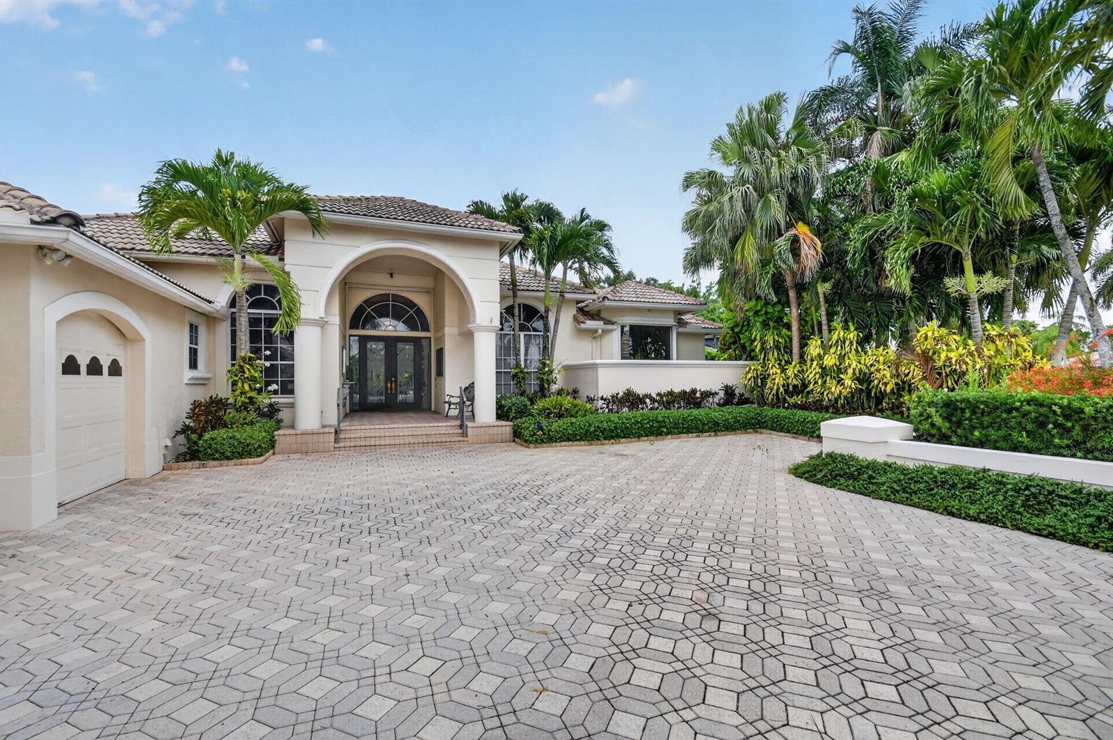A beige house with a paved driveway, arched entryway, and lush tropical landscaping — 4936 Exeter Estate Lane, Lake Worth FL 33449, LAKE WORTH, FL