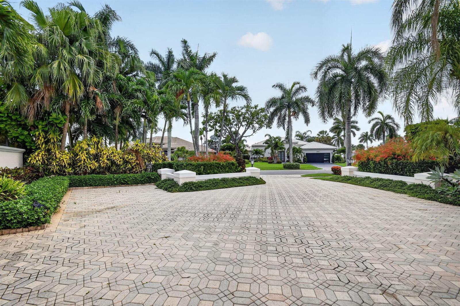 A paved driveway leads toward a house surrounded by lush tropical landscaping and palm trees — 4936 Exeter Estate Lane, Lake Worth FL 33449, LAKE WORTH, FL