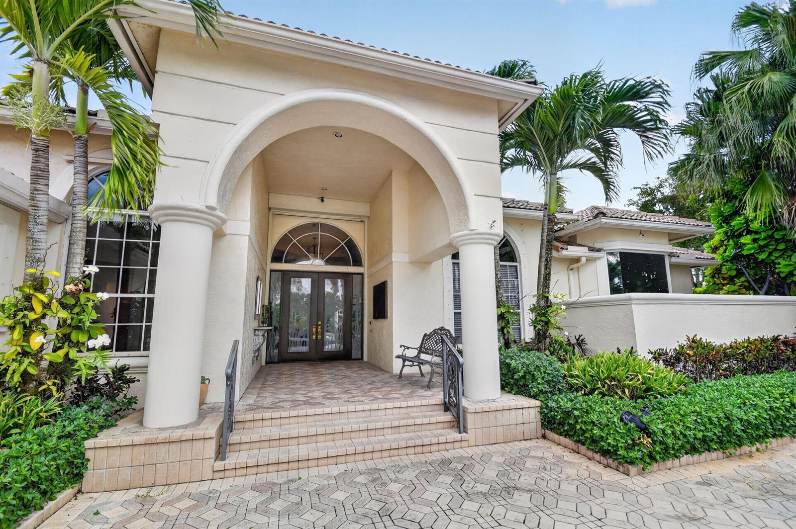 A beige house exterior features a covered arched entryway with columns and double glass doors — 4936 Exeter Estate Lane, Lake Worth FL 33449, LAKE WORTH, FL