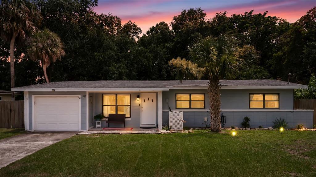 A single-story house with a white garage, gray siding, and a palm tree in front — 1717 WHITE STREET, TITUSVILLE, FL