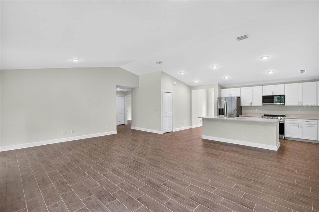 An open-concept living area features wood-look tile flooring, recessed lighting, and a modern white kitchen — 19112 RUSKIN AVENUE, PORT CHARLOTTE, FL