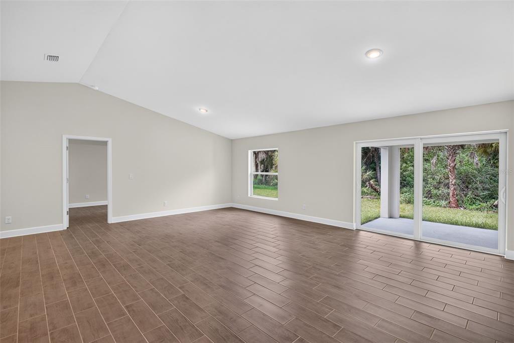 An empty living room features wood-look tile flooring, a vaulted ceiling, and sliding glass doors — 19112 RUSKIN AVENUE, PORT CHARLOTTE, FL