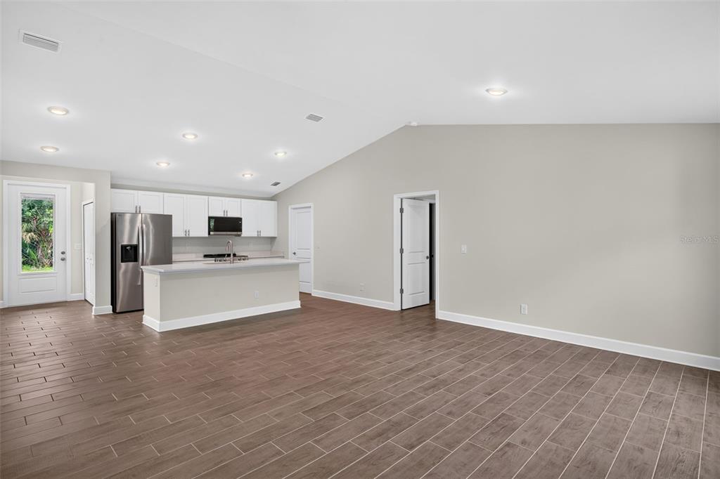 An open-concept kitchen and living area featuring white cabinets, stainless appliances, and wood-look tile flooring — 19112 RUSKIN AVENUE, PORT CHARLOTTE, FL