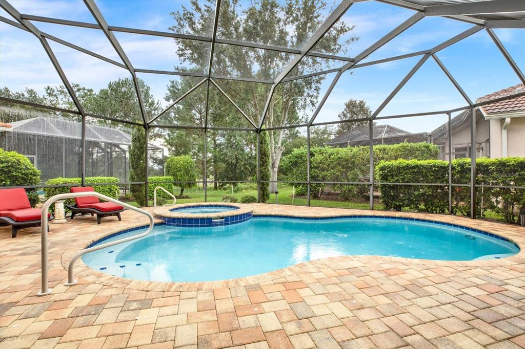 A screened-in swimming pool and spa with a brick paver deck and lounge chairs — 9004 JERICHO ROAD, WEEKI WACHEE, FL
