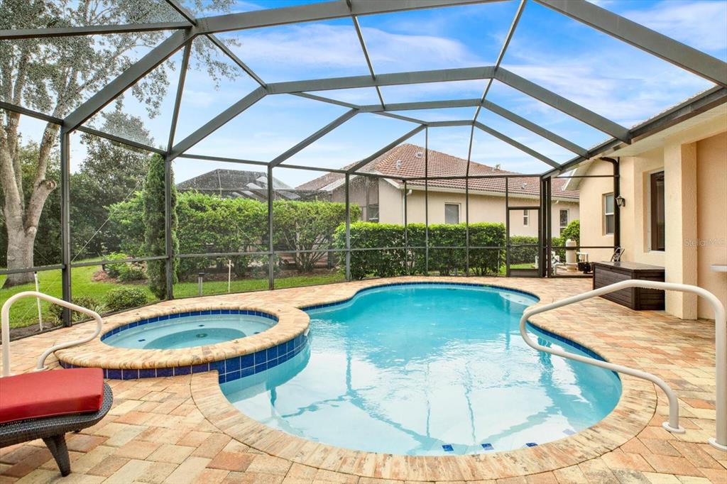 A screened-in patio features a swimming pool with an attached spa and paver decking — 9004 JERICHO ROAD, WEEKI WACHEE, FL