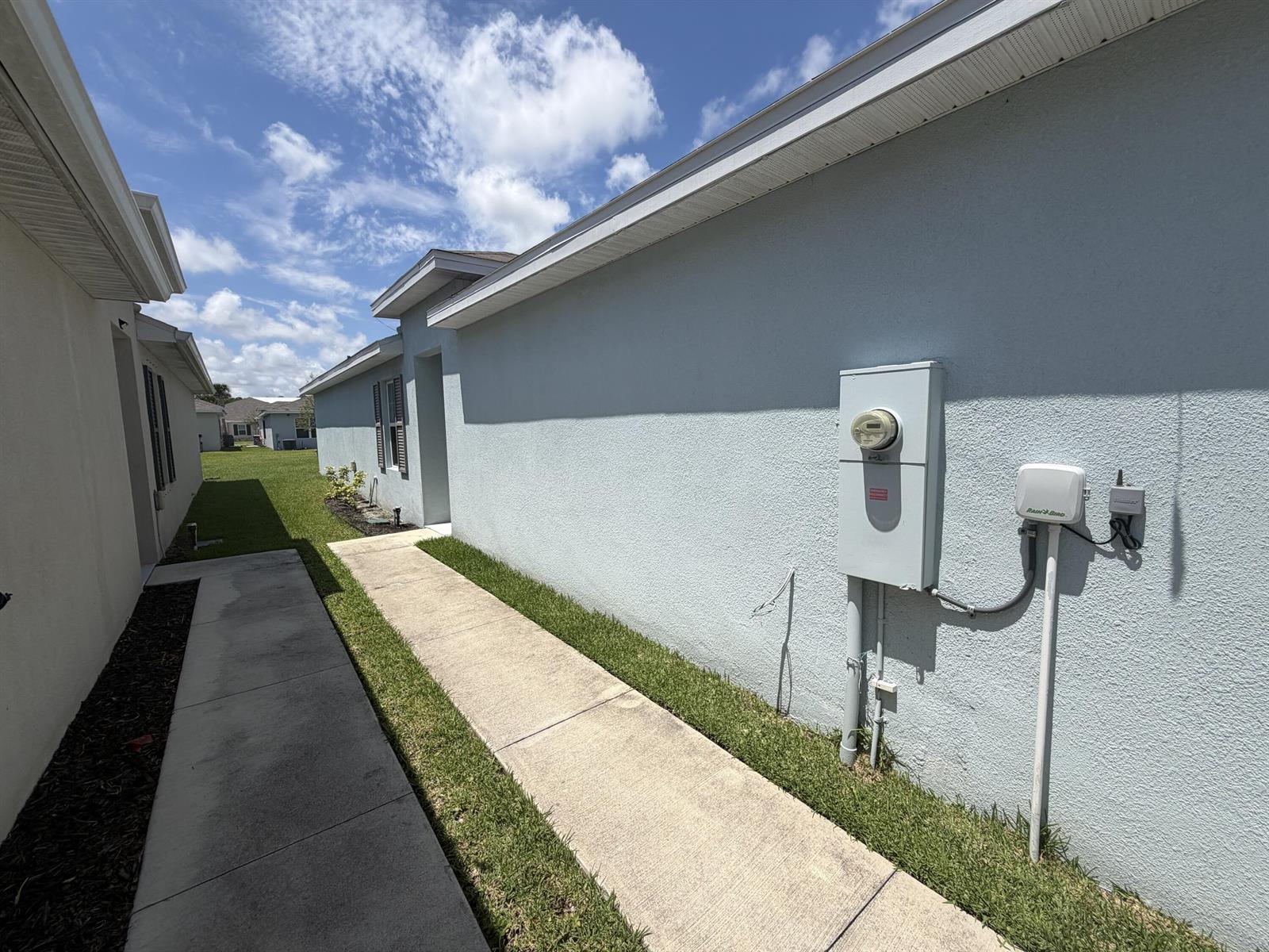 A view of a concrete walkway between two houses with an electrical meter and controller — 845 Persimmon Place, Fort Pierce FL 34981, FORT PIERCE, FL
