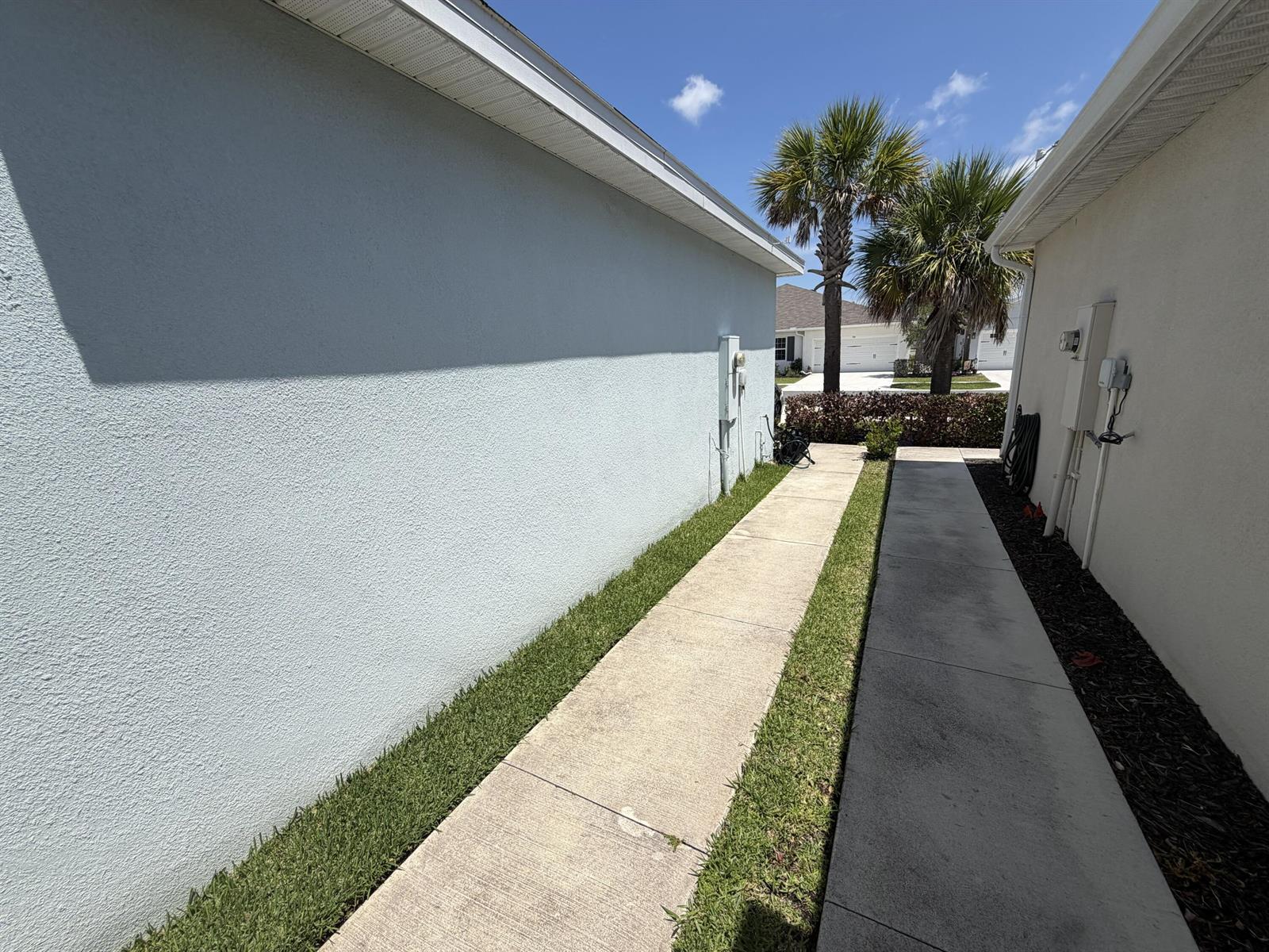 A narrow concrete walkway runs between two light-colored stucco exterior walls under a blue sky — 845 Persimmon Place, Fort Pierce FL 34981, FORT PIERCE, FL