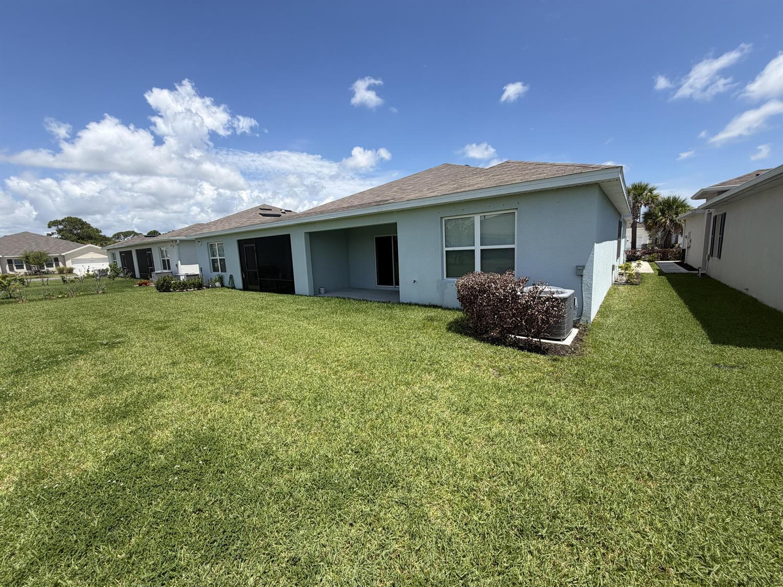 The backyard features a light-colored house with a covered patio and an air conditioning unit — 845 Persimmon Place, Fort Pierce FL 34981, FORT PIERCE, FL