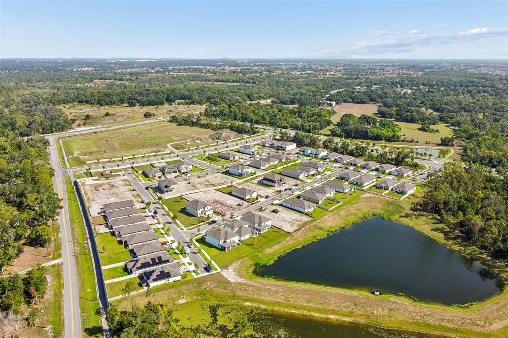 An aerial view shows a suburban neighborhood under construction with houses, roads, and a pond — 4910 MEADOW BAY COURT, WIMAUMA, FL