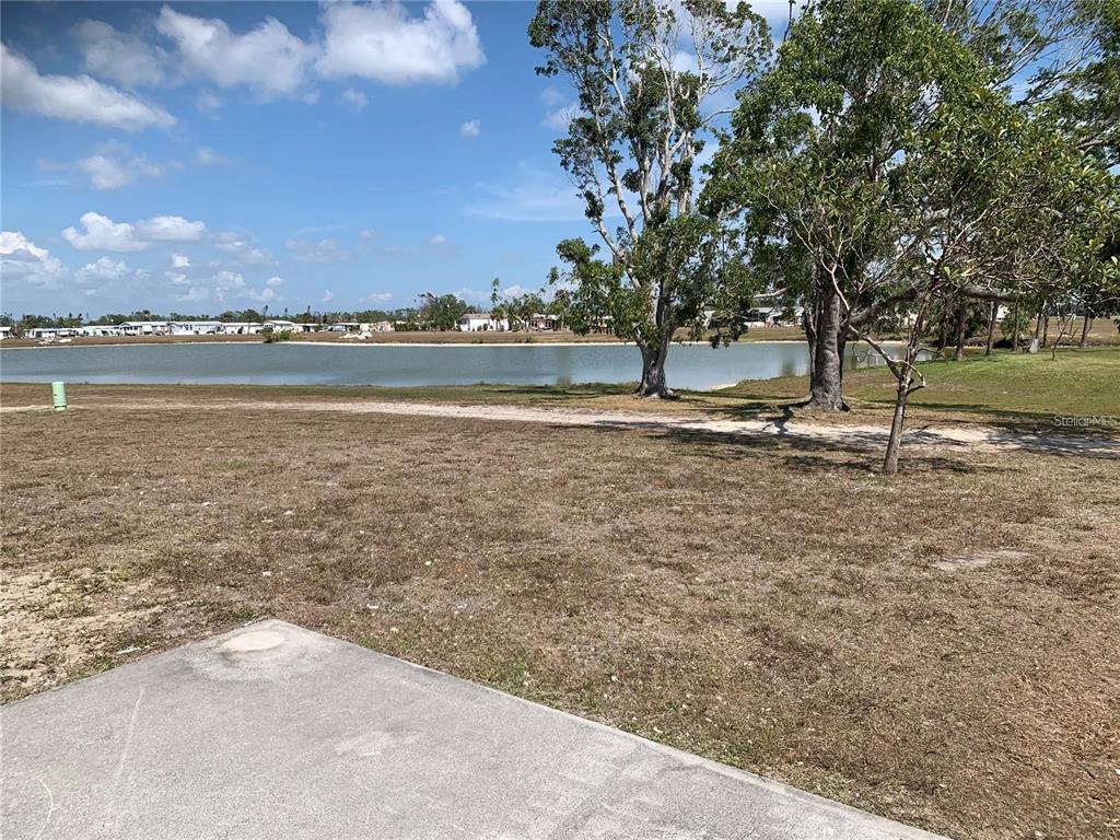 A concrete slab overlooks a grassy lot and a pond under a blue sky — 7578 RATAN CIRCLE, PORT CHARLOTTE, FL