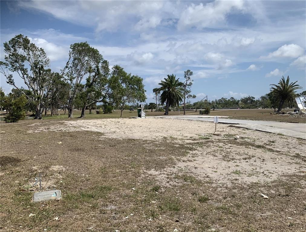 A vacant, sandy residential lot features a concrete driveway, utility hookups, and scattered palm trees — 7578 RATAN CIRCLE, PORT CHARLOTTE, FL