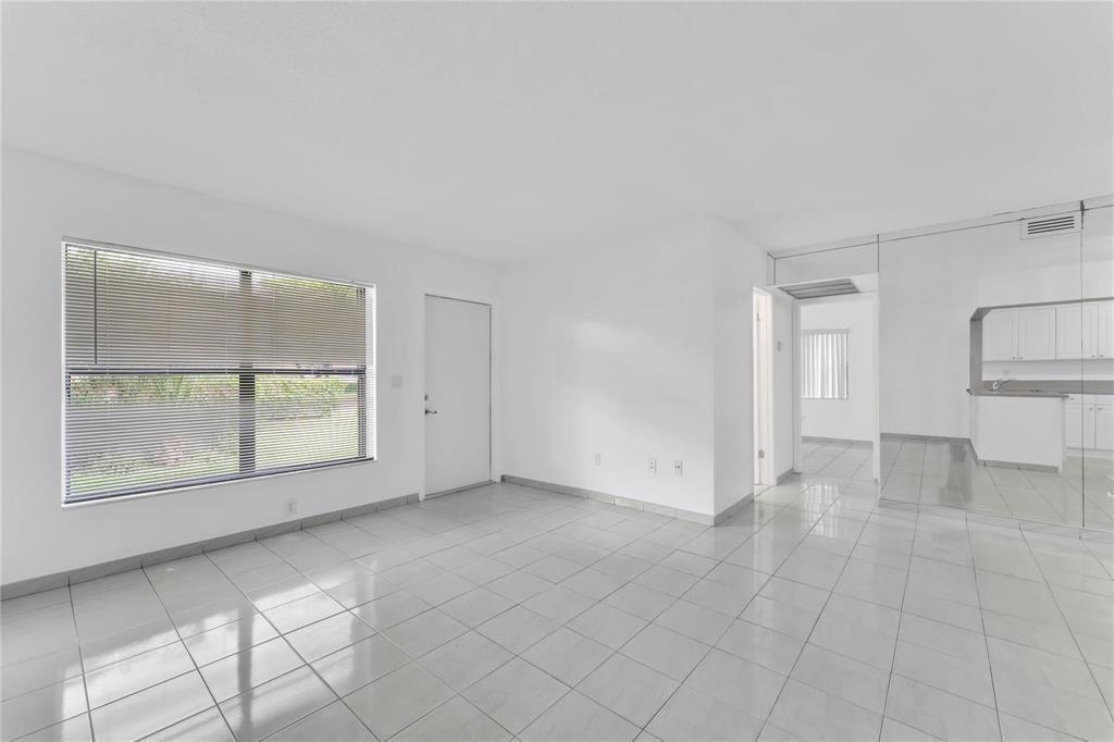 A bright, empty room features white walls, light-colored tile flooring, and a large window — 6705 W 26th Drive # 7, Hialeah FL 33016, HIALEAH, FL