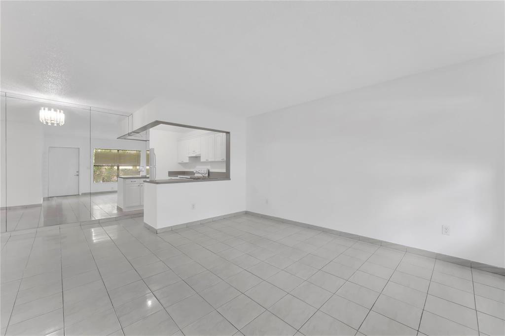 A living area with light tile flooring, a mirrored wall, and an open kitchen pass-through — 6705 W 26th Drive # 7, Hialeah FL 33016, HIALEAH, FL
