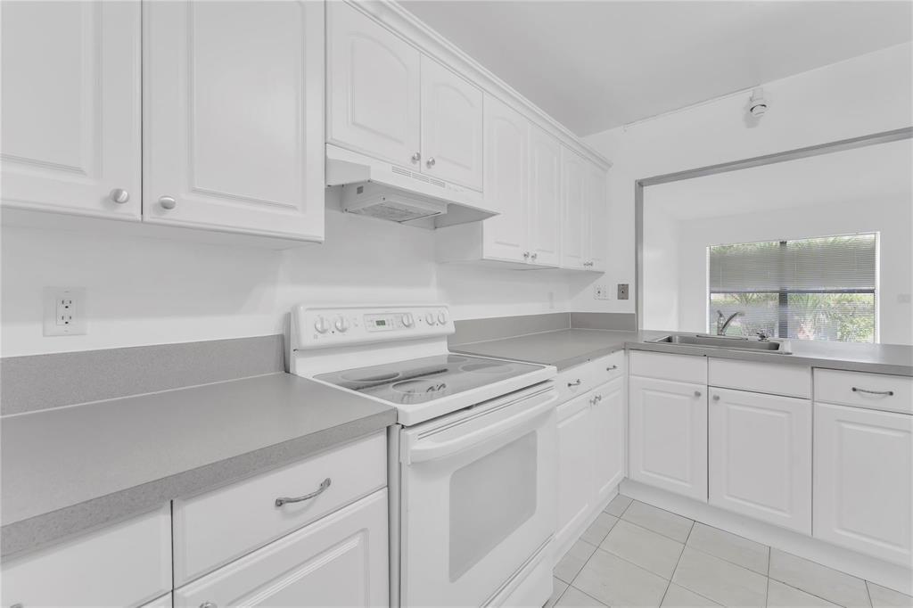 A white kitchen features gray laminate countertops, white cabinetry, and a white electric range — 6705 W 26th Drive # 7, Hialeah FL 33016, HIALEAH, FL