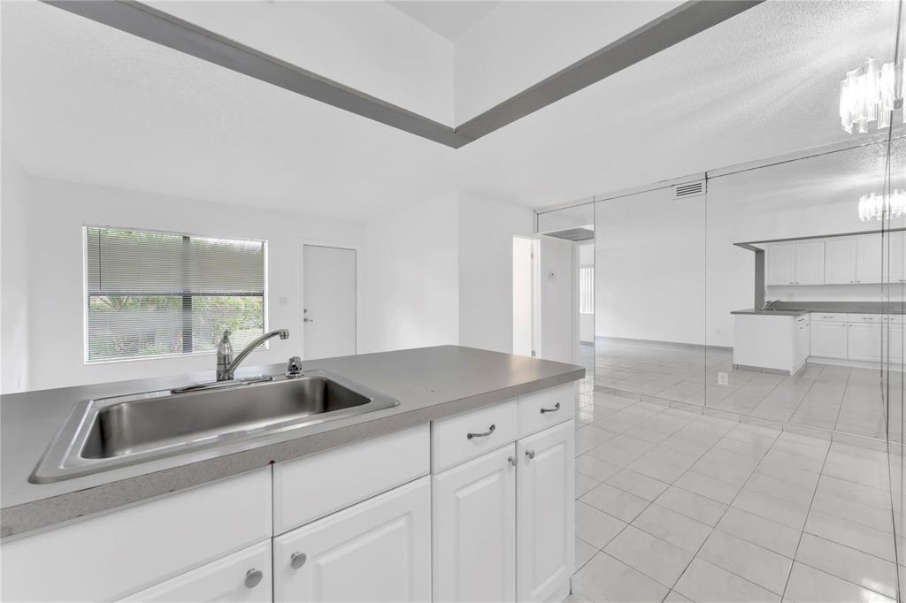 A kitchen island with a stainless steel sink sits in a room with white cabinets — 6705 W 26th Drive # 7, Hialeah FL 33016, HIALEAH, FL