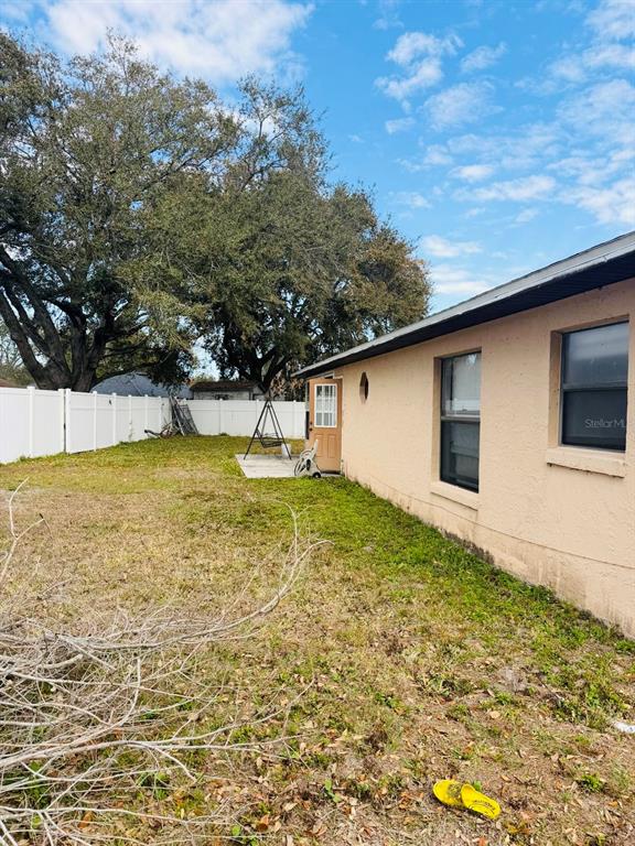 A view of a backyard with a tan house exterior, a white fence, and trees — 2910 VIENNA LANE, KISSIMMEE, FL
