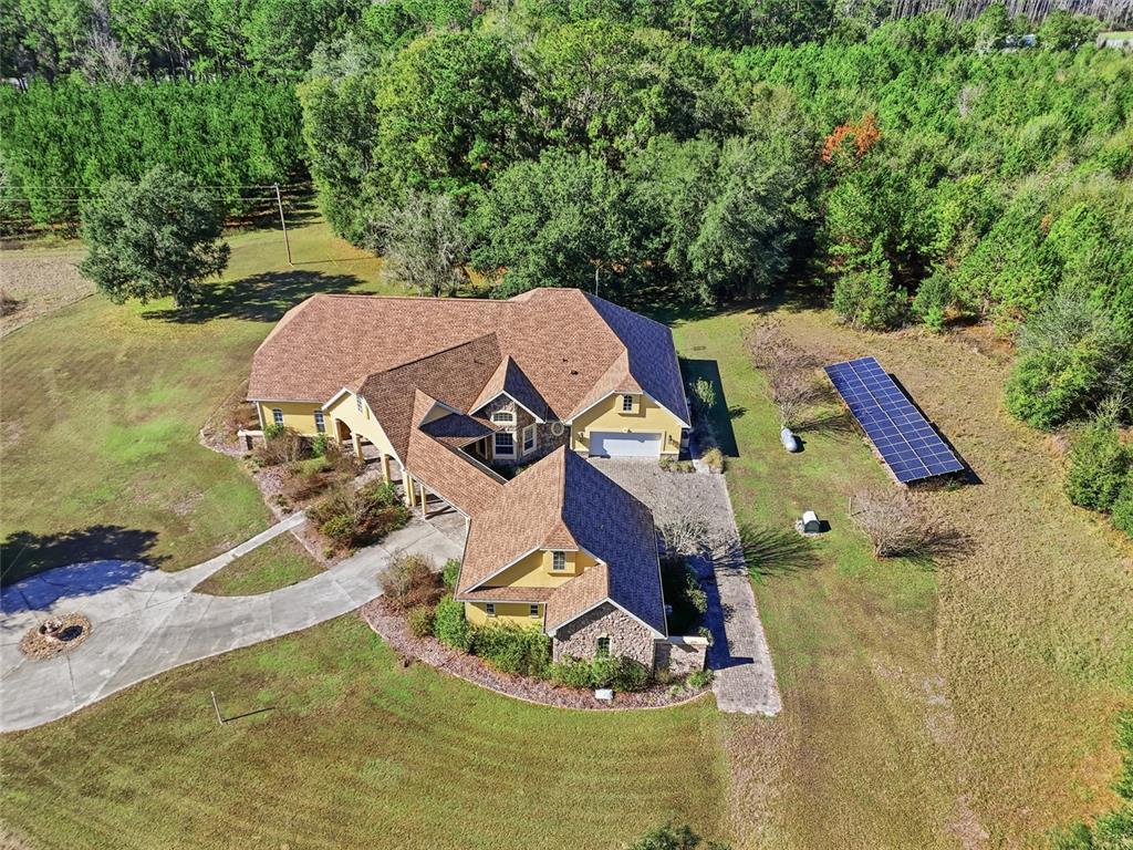 An aerial view shows a yellow house with a brown roof and ground-mounted solar panels — 18604 NW 262 AVENUE, ALACHUA, FL