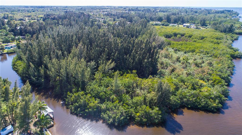 An aerial view shows a dense wooded lot bordered by a canal and a river — 418 PEACE ISLAND DR, PUNTA GORDA, FL