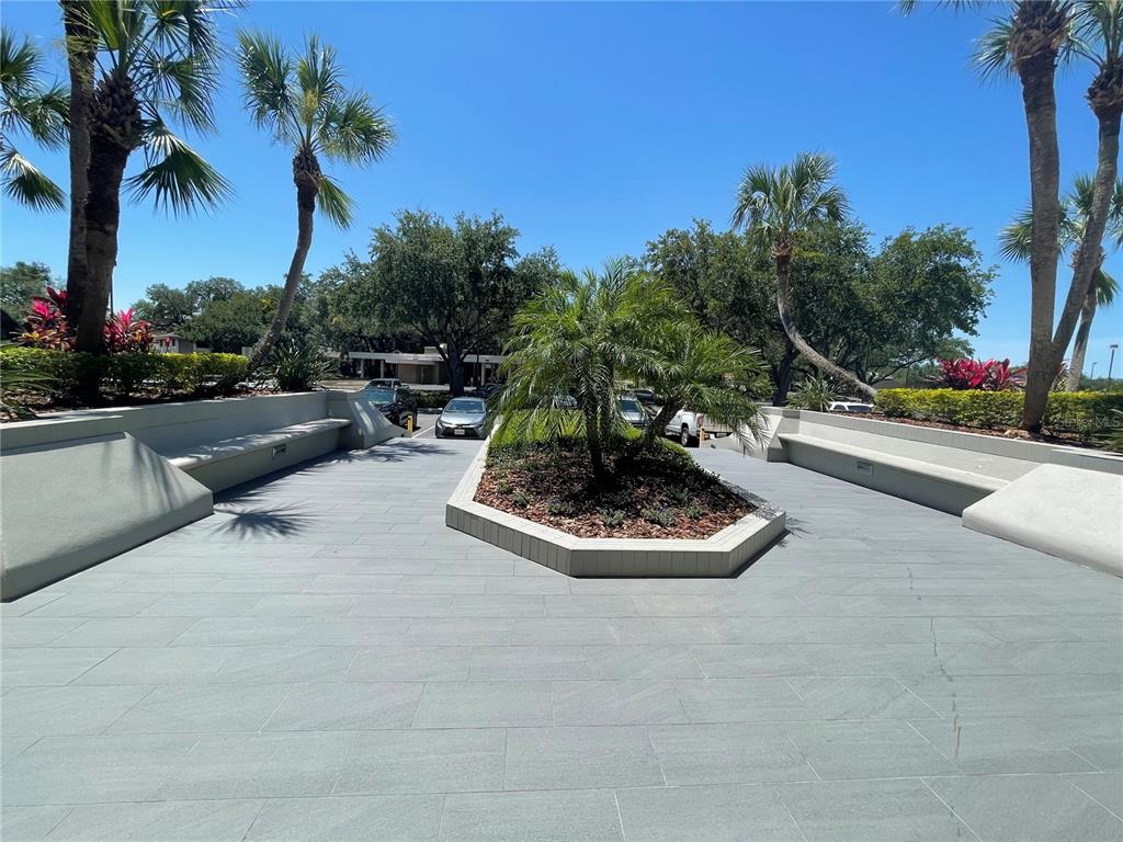 A paved outdoor courtyard features a central planter with a palm tree and built-in benches — 1300 CITIZENS BOULEVARD, LEESBURG, FL