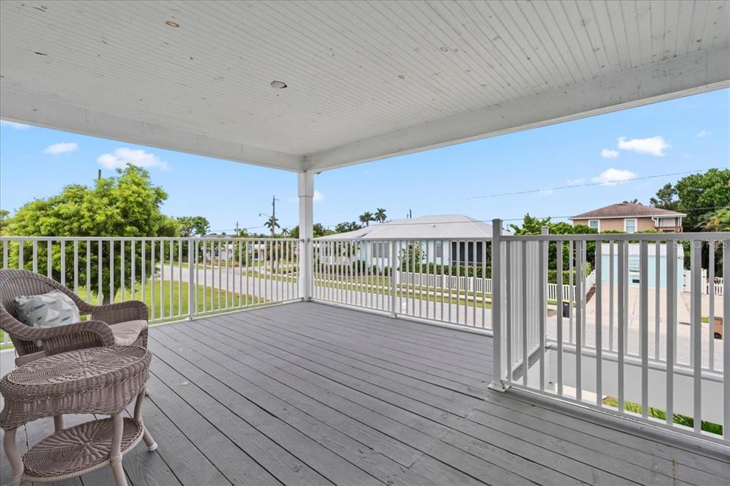 A covered wooden deck features white railings and wicker furniture overlooking a residential street — 1306 MCGREGOR STREET, PUNTA GORDA, FL