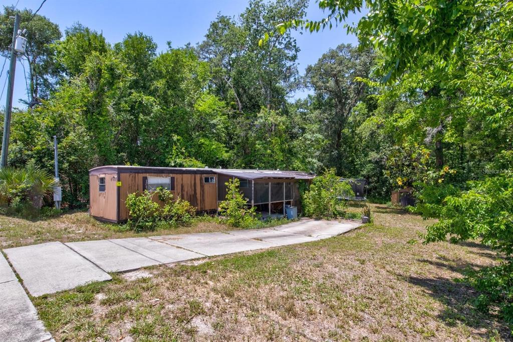 A brown mobile home with a screened porch sits on a lot with mature trees — 4750 N RONALD REAGAN BOULEVARD, SANFORD, FL