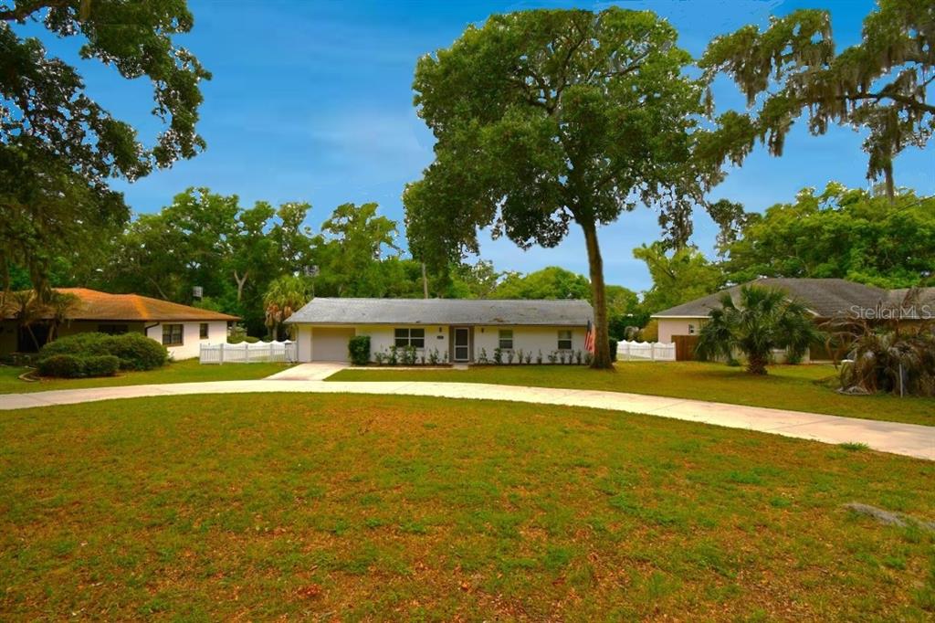 A single-story house with a white exterior and a curved driveway sits under large trees — 2898 ALAMEDA DEL NORTE, EUSTIS, FL