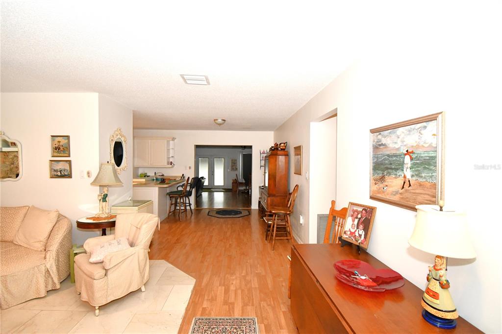 A living room with light wood-look flooring leads to a kitchen and a back doorway — 2898 ALAMEDA DEL NORTE, EUSTIS, FL