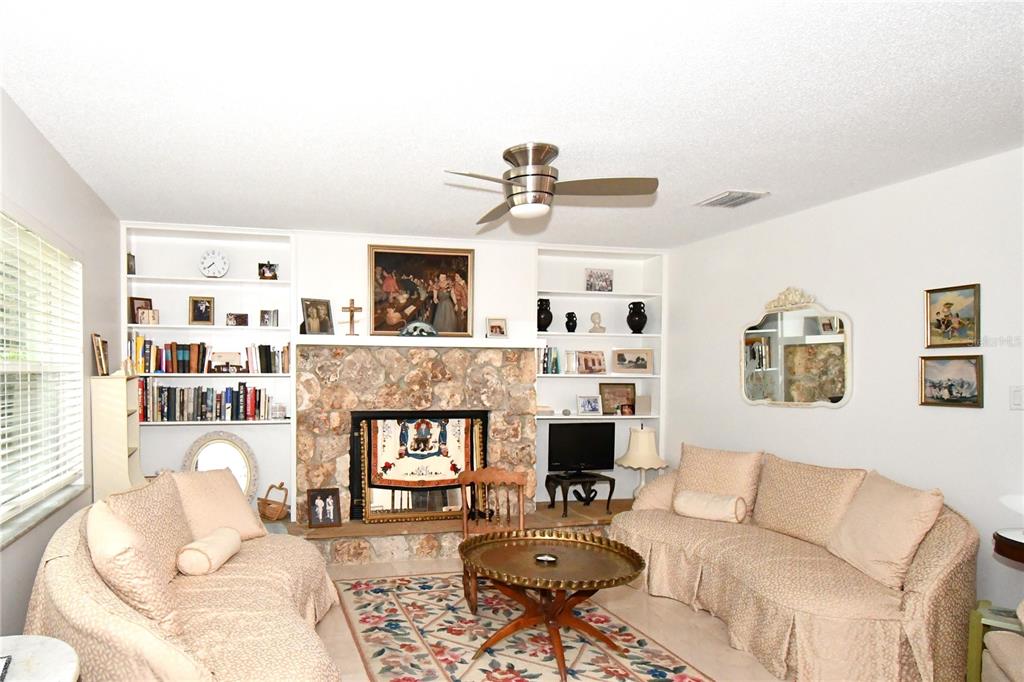 A living room features a stone fireplace, built-in shelving, two beige sofas, and a ceiling fan — 2898 ALAMEDA DEL NORTE, EUSTIS, FL