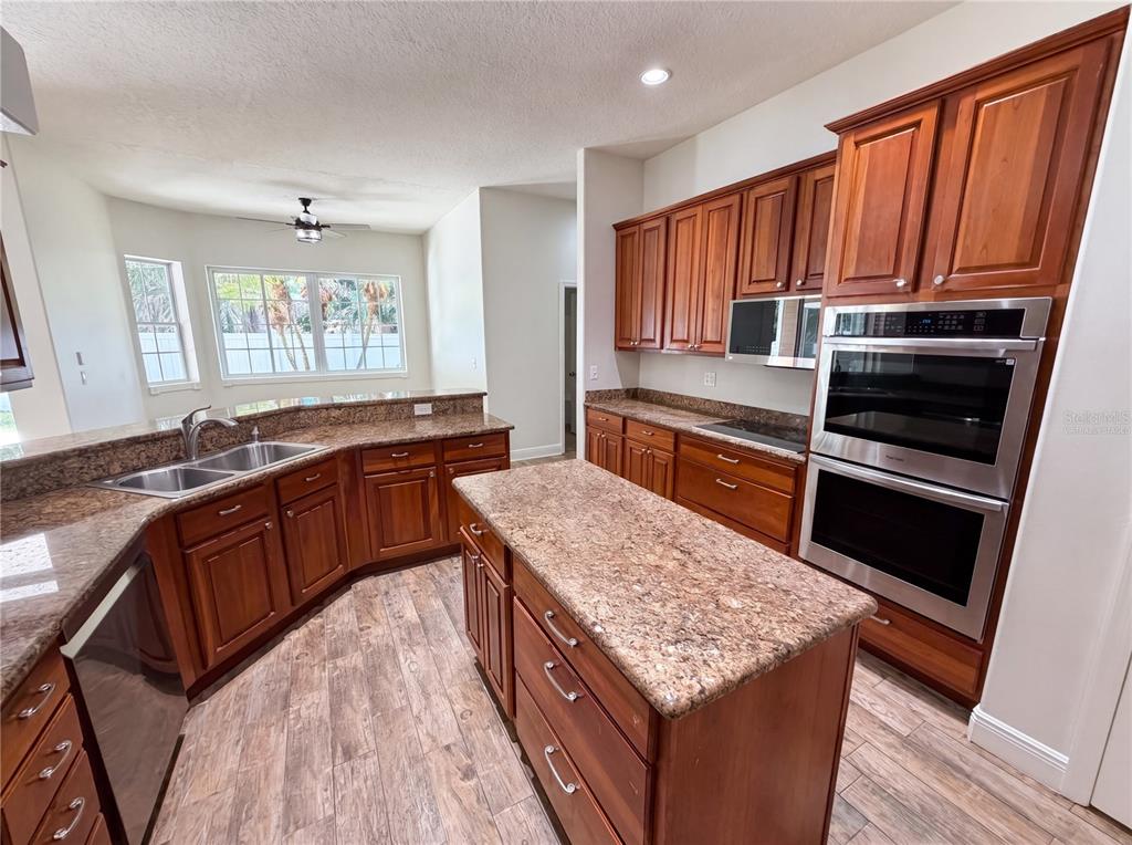 A kitchen features wood cabinets, granite countertops, stainless steel appliances, and wood-look tile flooring — 375 NORA AVENUE, MERRITT ISLAND, FL