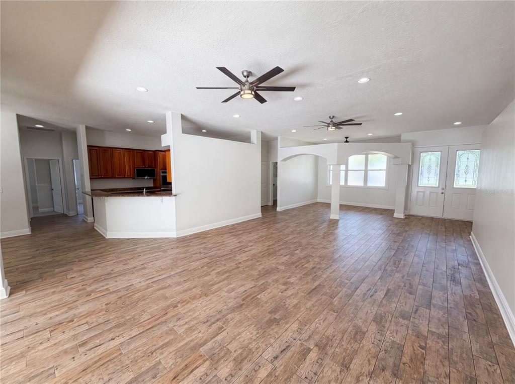 An open-concept living area features wood-look tile flooring, two ceiling fans, and a kitchen — 375 NORA AVENUE, MERRITT ISLAND, FL