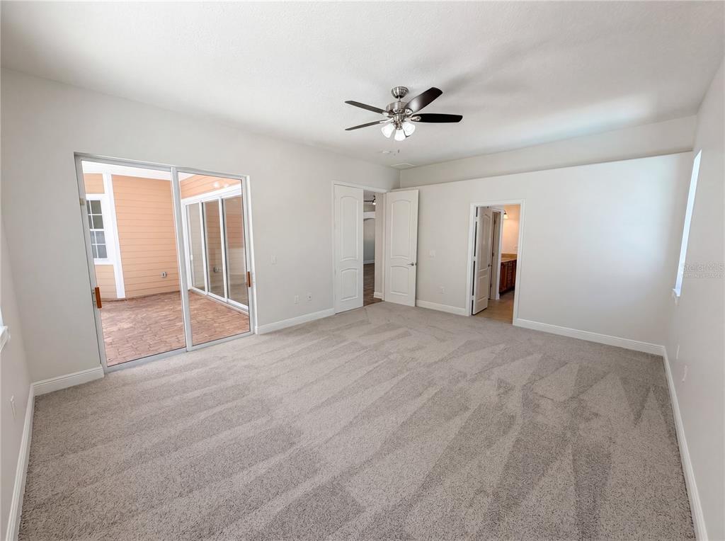 A bedroom with gray carpet, a ceiling fan, sliding glass doors, and two doorways — 375 NORA AVENUE, MERRITT ISLAND, FL