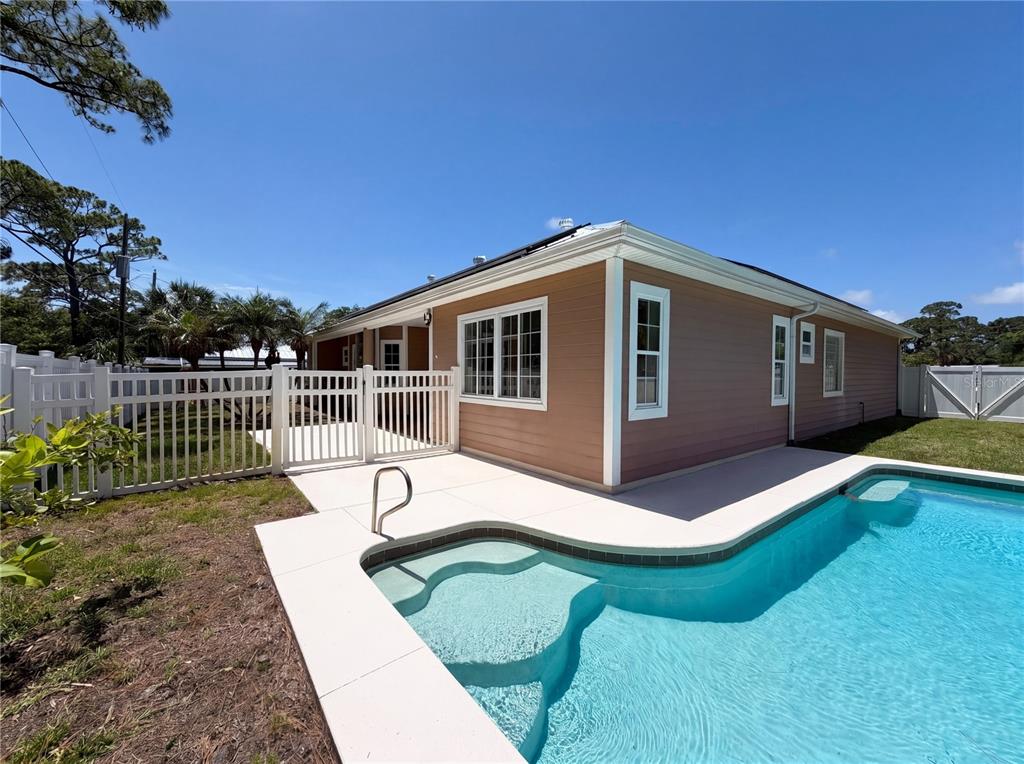 A tan house with white trim features a swimming pool and a white vinyl fence — 375 NORA AVENUE, MERRITT ISLAND, FL