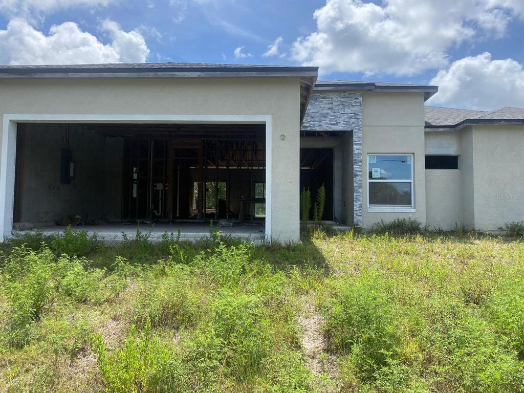 An unfinished house exterior features a large open-framed patio area and stone veneer accents — 10035 HACKENSACK STREET, PORT CHARLOTTE, FL