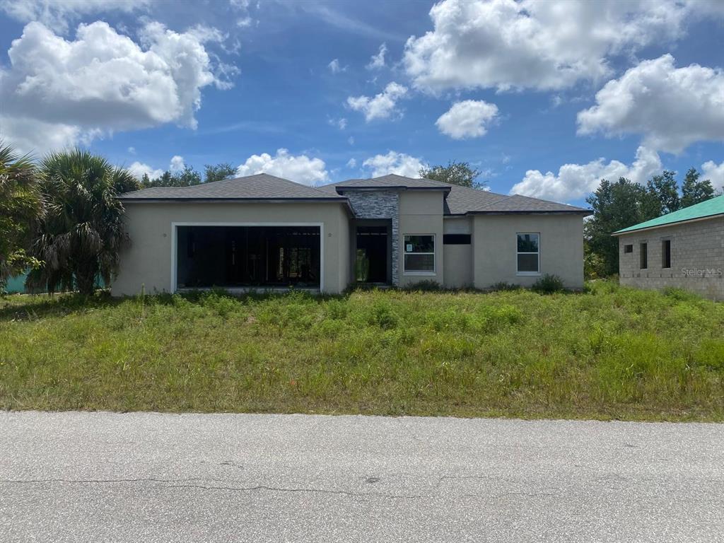 A single-story house under construction with a garage, stone accent, and overgrown front yard — 10035 HACKENSACK STREET, PORT CHARLOTTE, FL