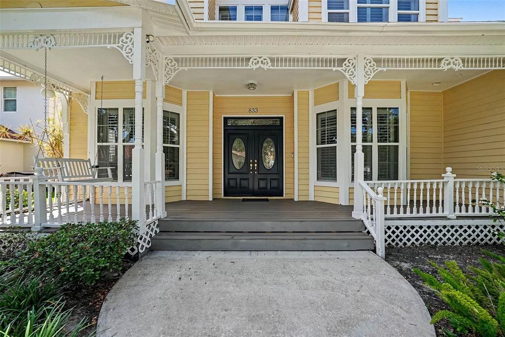 A yellow house features a covered front porch with a swing and double entry doors — 833 MARCO DRIVE NE, ST PETERSBURG, FL