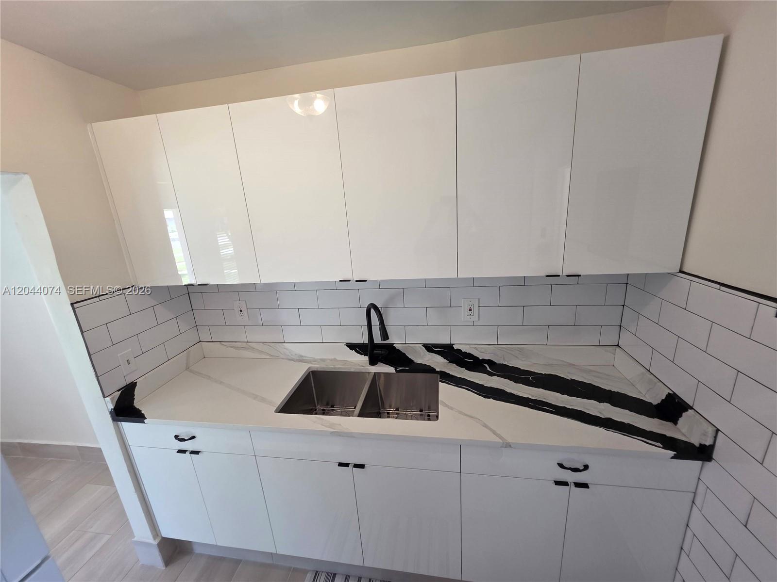 A kitchen features white cabinets, a black-veined marble countertop, and a white subway tile backsplash — 120 NE 10th Ave # 3, Hallandale Beach FL 33009, HALLANDALE BEACH, FL