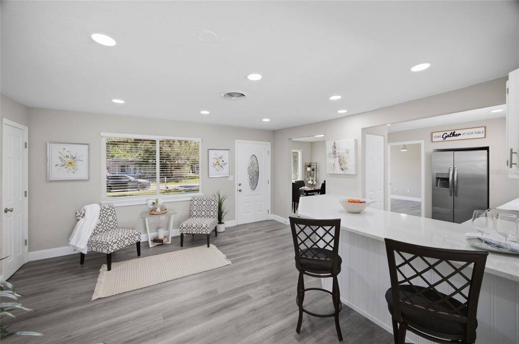 A bright kitchen and living area featuring gray wood-look flooring, white cabinetry, and bar seating — 923 N PALM DRIVE SW, LARGO, FL