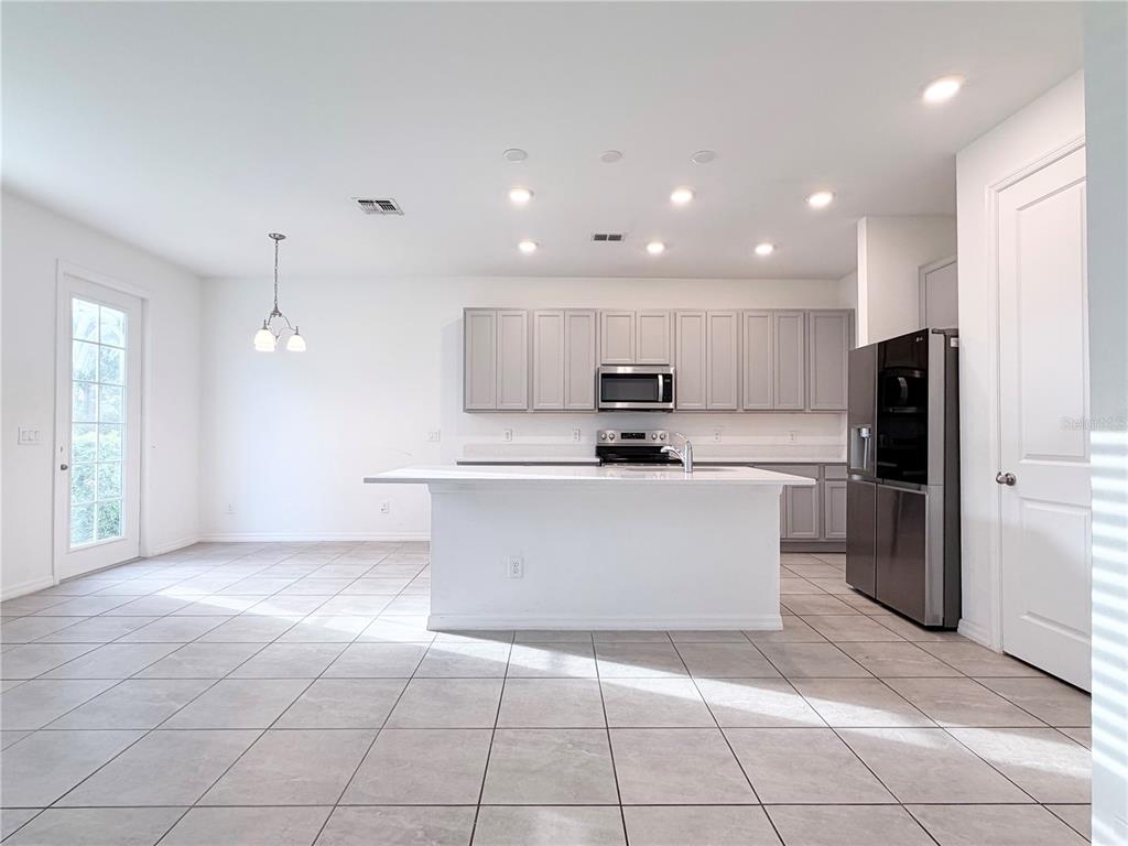 A kitchen features gray cabinets, a white island, stainless steel appliances, and light tile flooring — 1542 DISCOVERY STREET, DAVENPORT, FL
