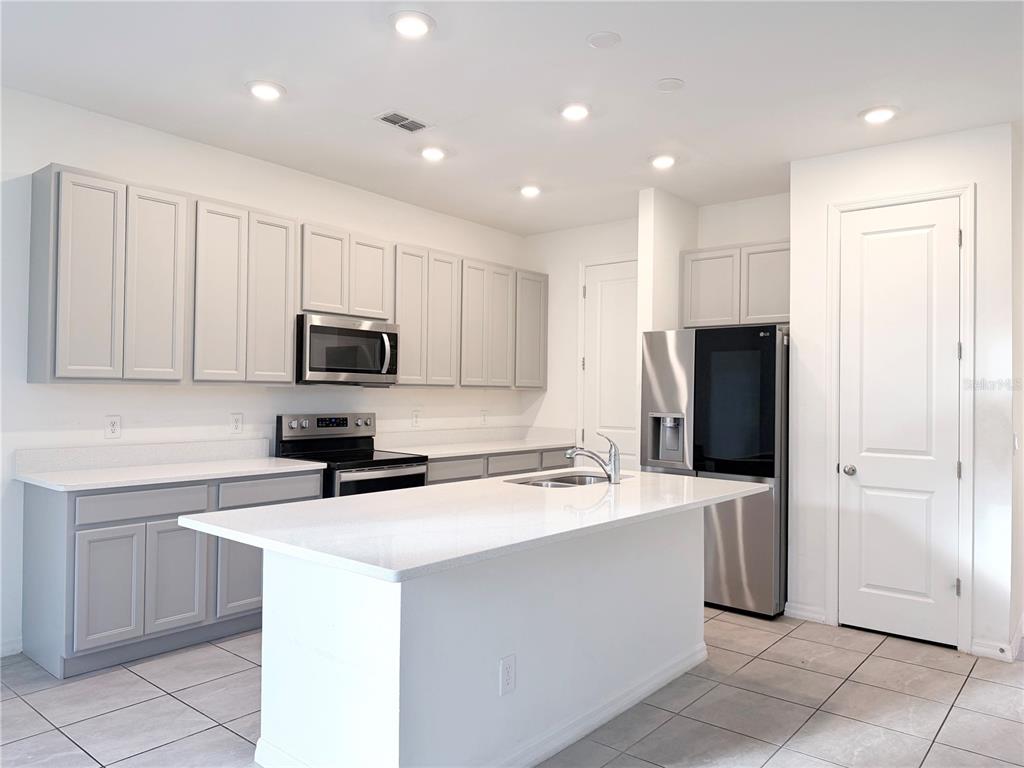 A kitchen features light gray cabinets, white countertops, a central island, and stainless steel appliances — 1542 DISCOVERY STREET, DAVENPORT, FL