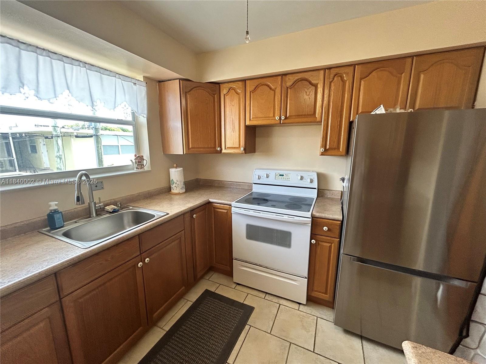 A kitchen features wood cabinets, a stainless steel refrigerator, a white stove, and tile flooring — 1717 Rodman St # 15, Hollywood FL 33020, HOLLYWOOD, FL