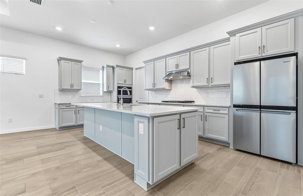 A modern kitchen features light gray cabinets, a large white island, and stainless steel appliances — 13630 CANYON RIDGE ROAD, SPRING HILL, FL