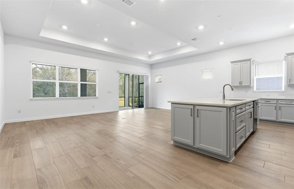 A bright, open-concept kitchen and living area featuring light wood-look tile flooring and grey cabinetry — 13630 CANYON RIDGE ROAD, SPRING HILL, FL